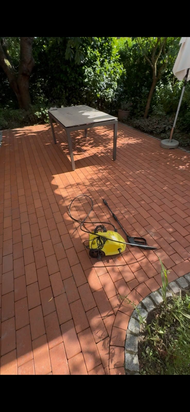 Terrasse aus rotem Klinker nach der Reinigung, daneben der Hochdruckreiniger